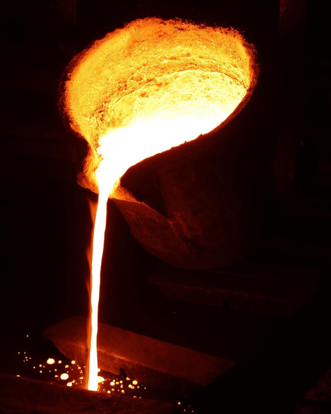 Molten metal being poured from a crucible into a mold during a high-temperature metal casting process in a foundry.