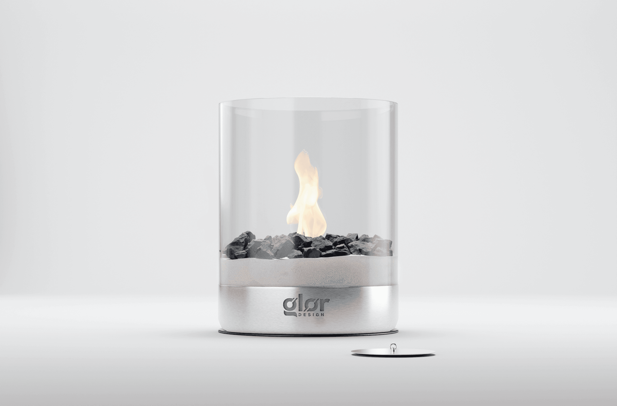 Modern tabletop fireplace with a cylindrical glass enclosure, black decorative stones, and a visible flame, set on a sleek silver base labeleddsr DESIGN.