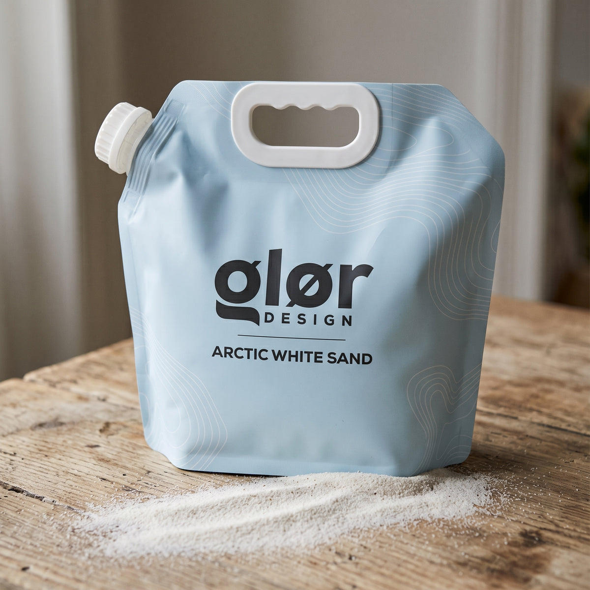 glør Arctic White Sand pouch on a wooden table with the fine white sand poured out beside it