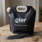 glør Volcano Black Sand pouch on a wooden table with the fine black sand poured out beside it